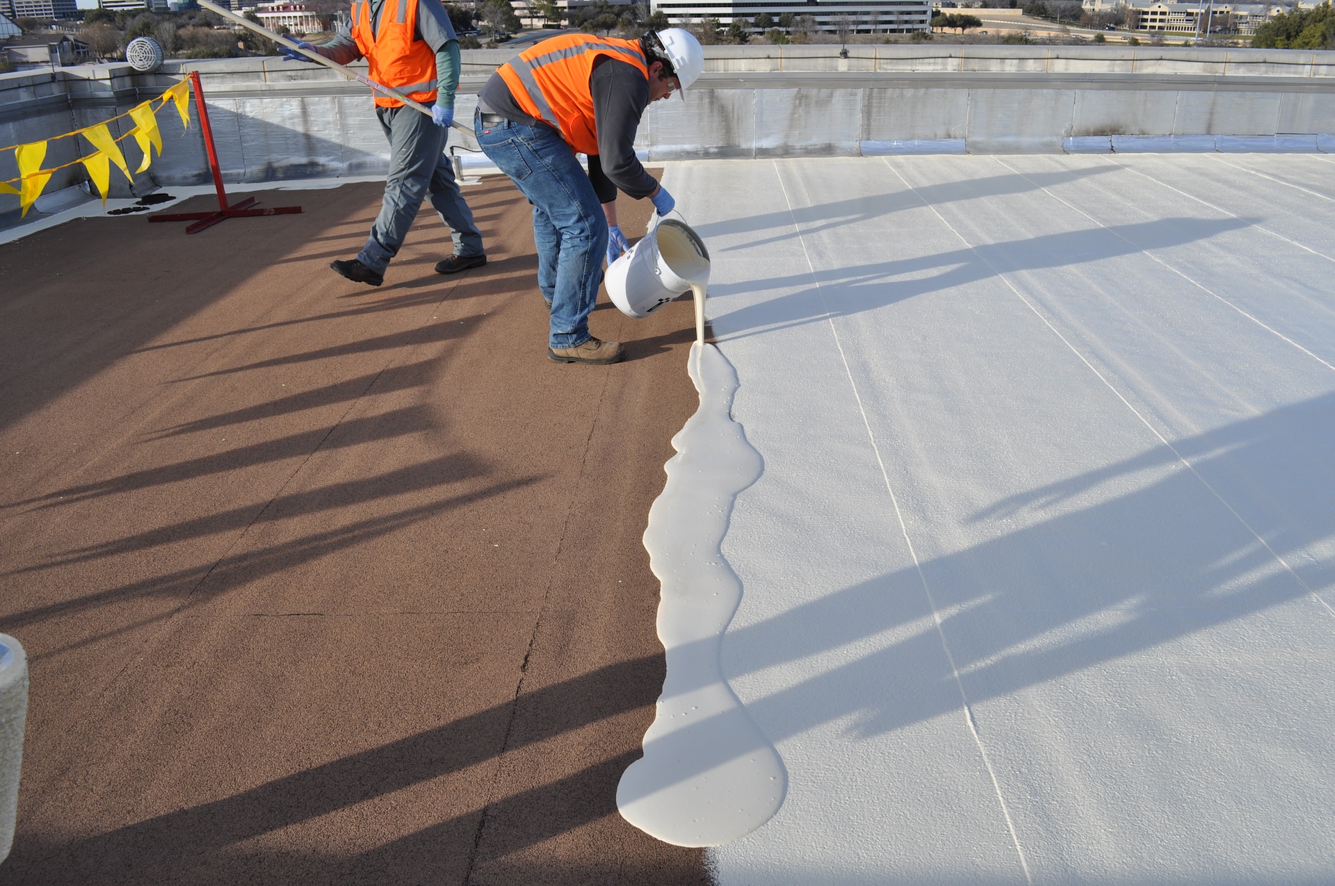 Commercial roof surface prepared with white coating and buckets of adhesive during deck installation.